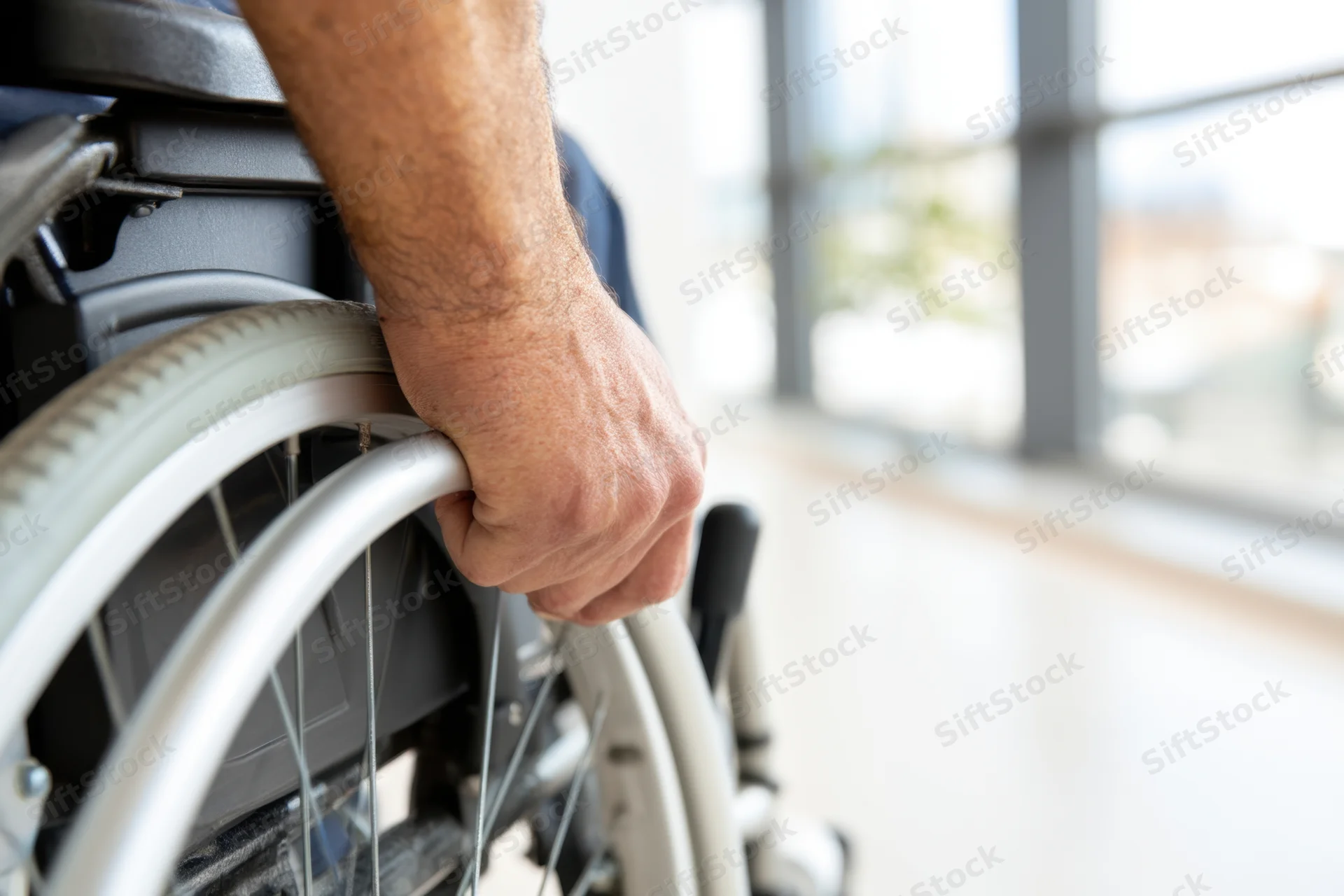 Man’s hand gripping wheelchair wheel indoors near window