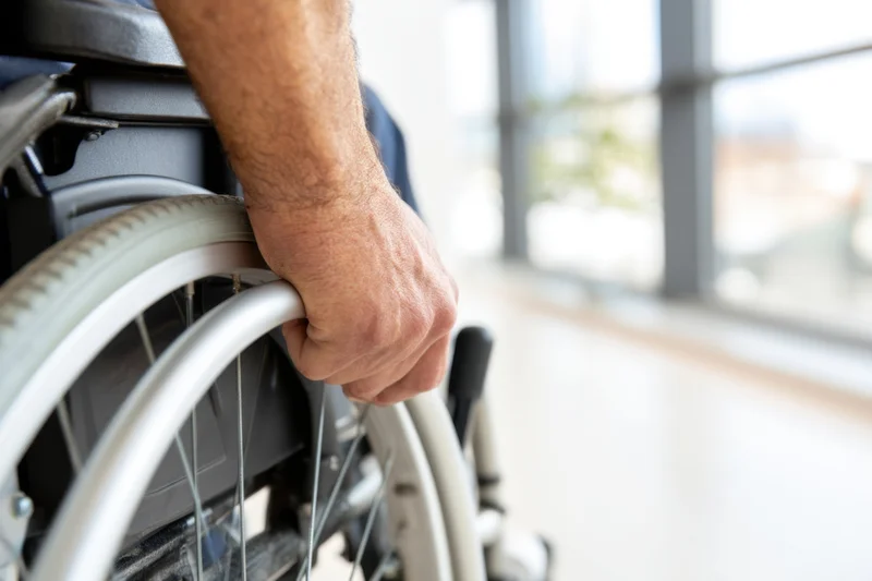 Man’s hand gripping wheelchair wheel indoors near window
