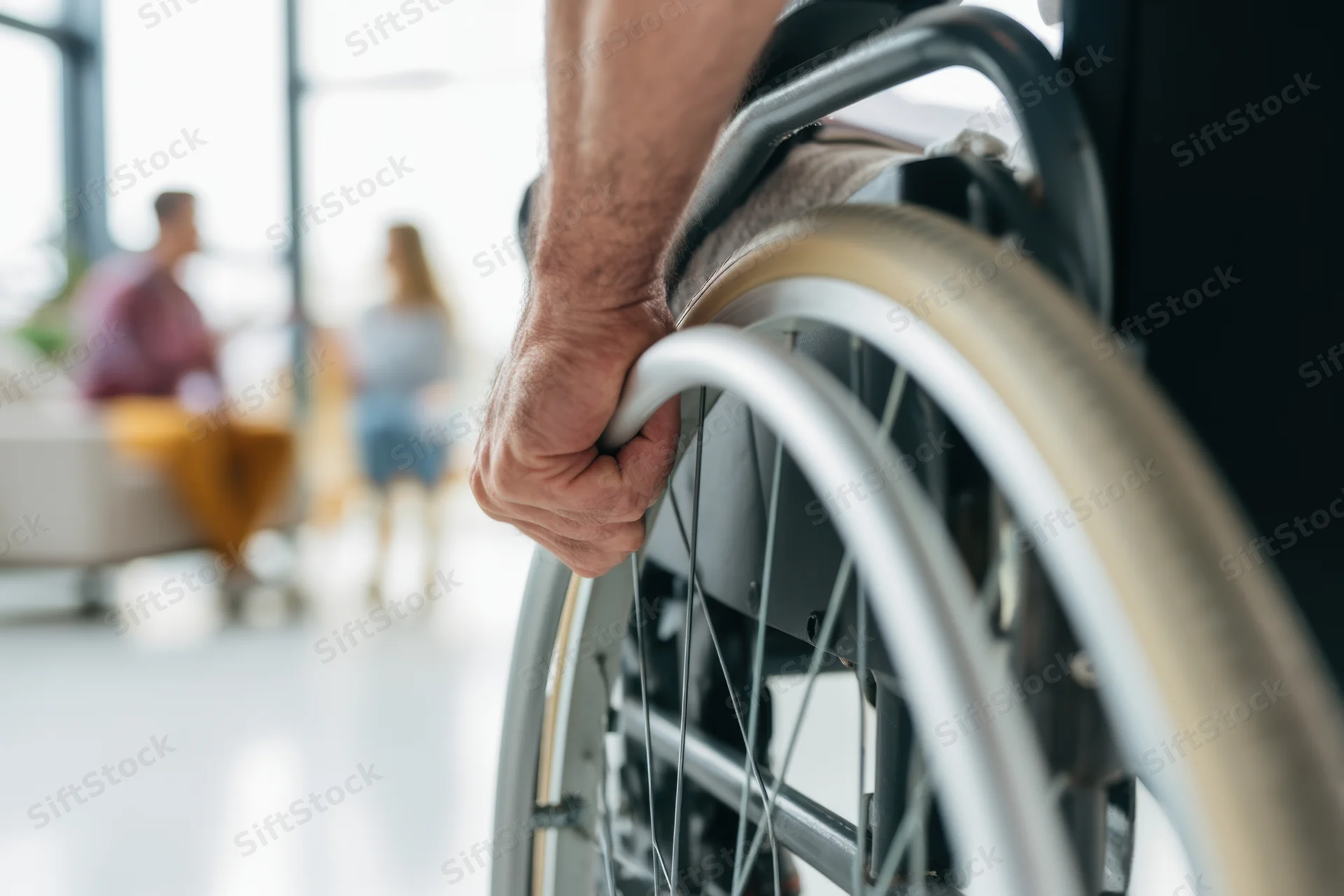 Close-up of a man's hand gripping the wheel of a wheelchair in a modern office setting