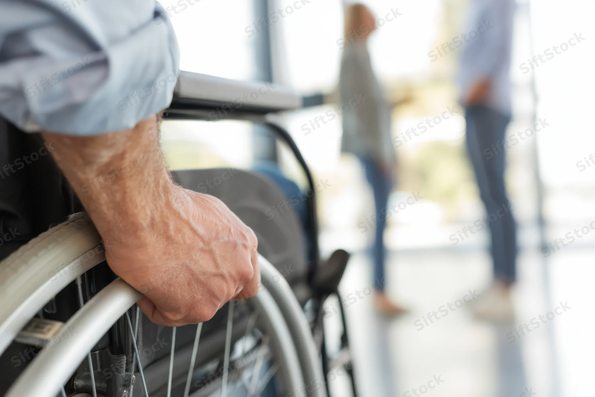 Close-up of a senior man's hand gripping a wheelchair wheel in a hospital corridor