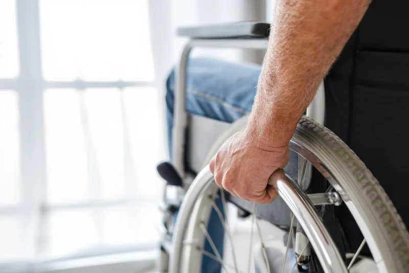 Close-up of a man's hand gripping the wheel of a wheelchair indoors near a window