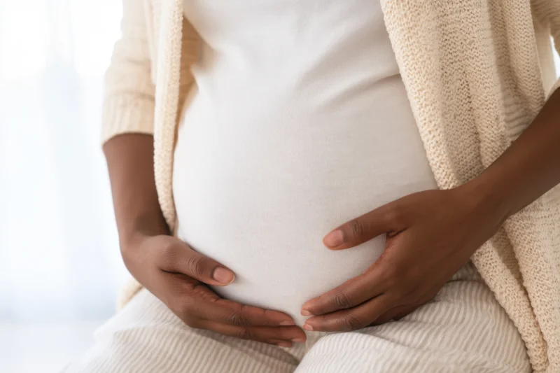 Pregnant woman cradling her belly with hands while seated indoors