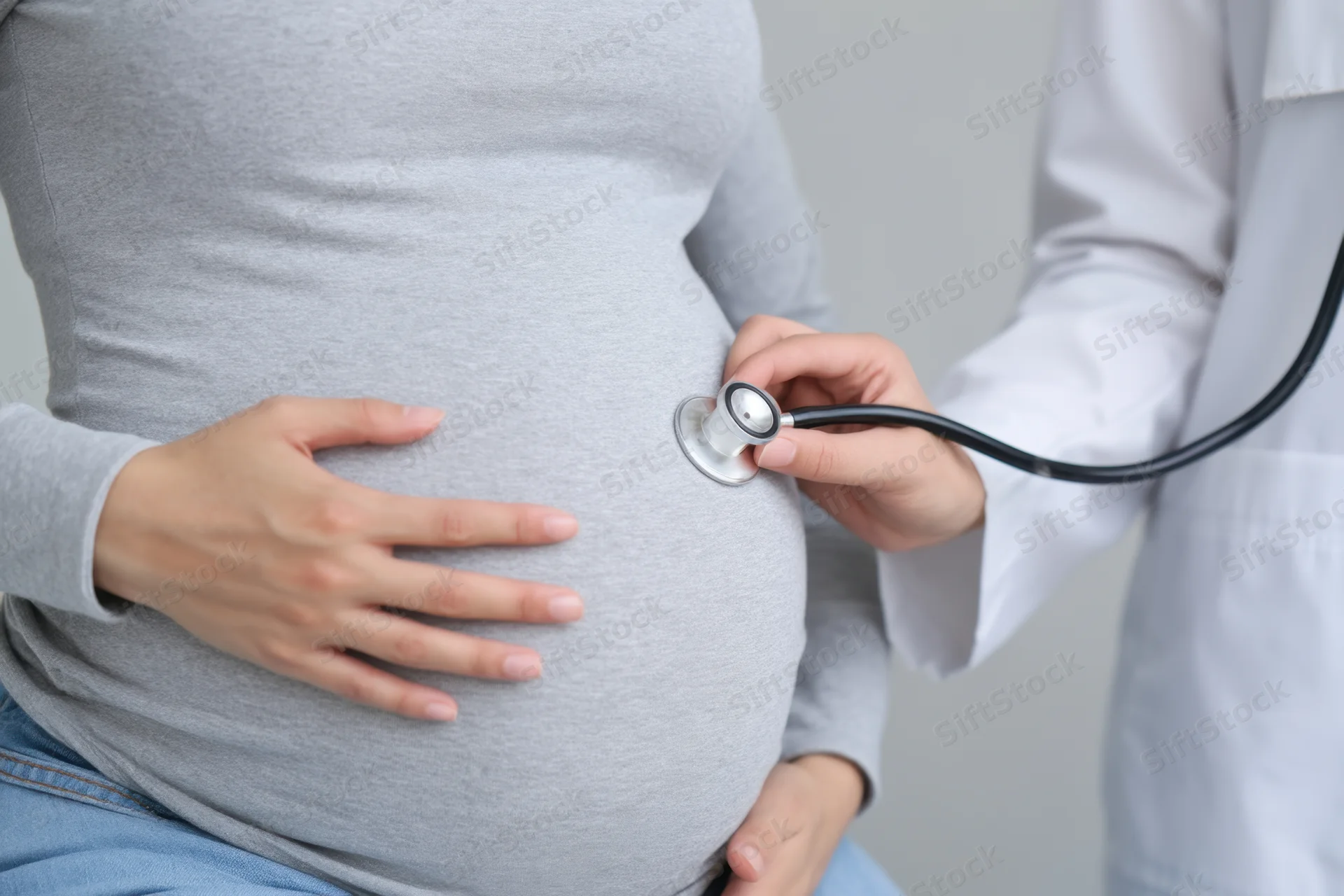 Pregnant woman with doctor using stethoscope on her belly during medical checkup