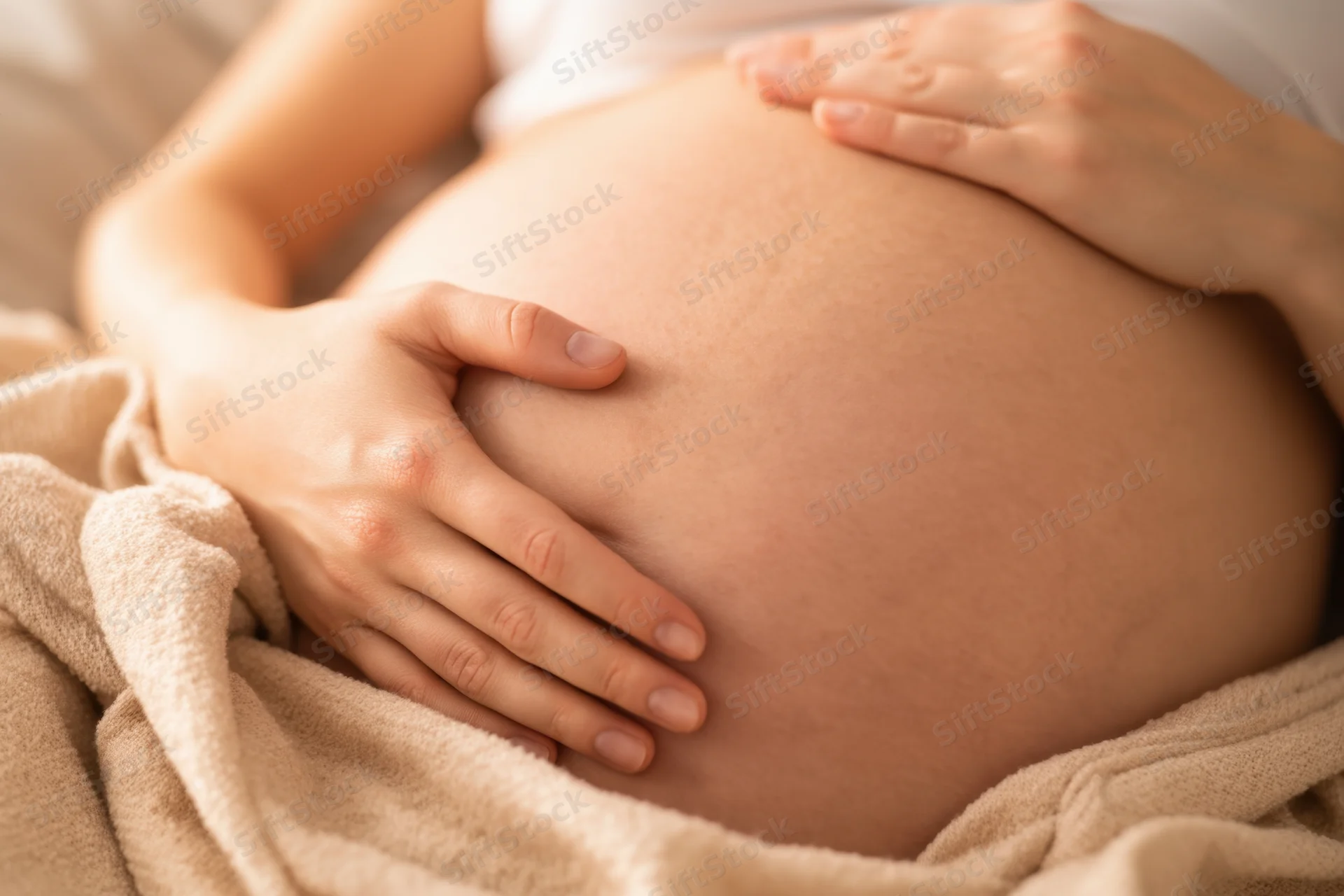 Pregnant woman cradling her belly with hands while lying on a blanket in bed