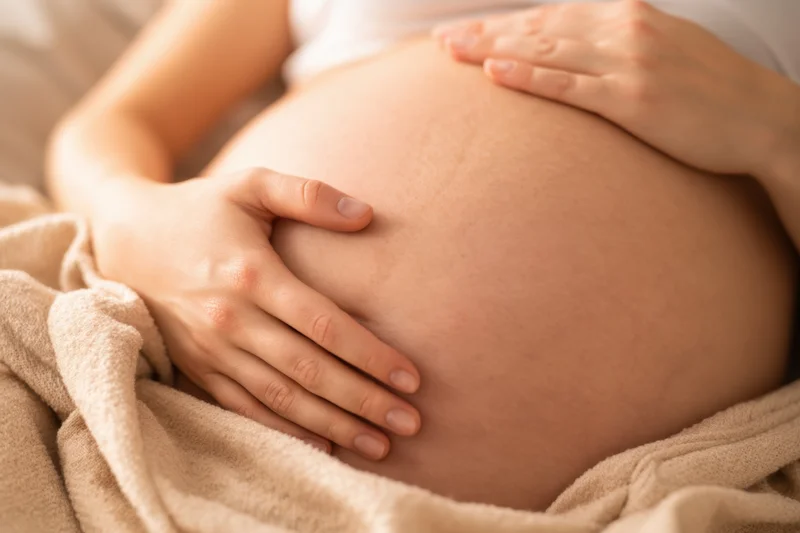 Pregnant woman cradling her belly with hands while lying on a blanket in bed
