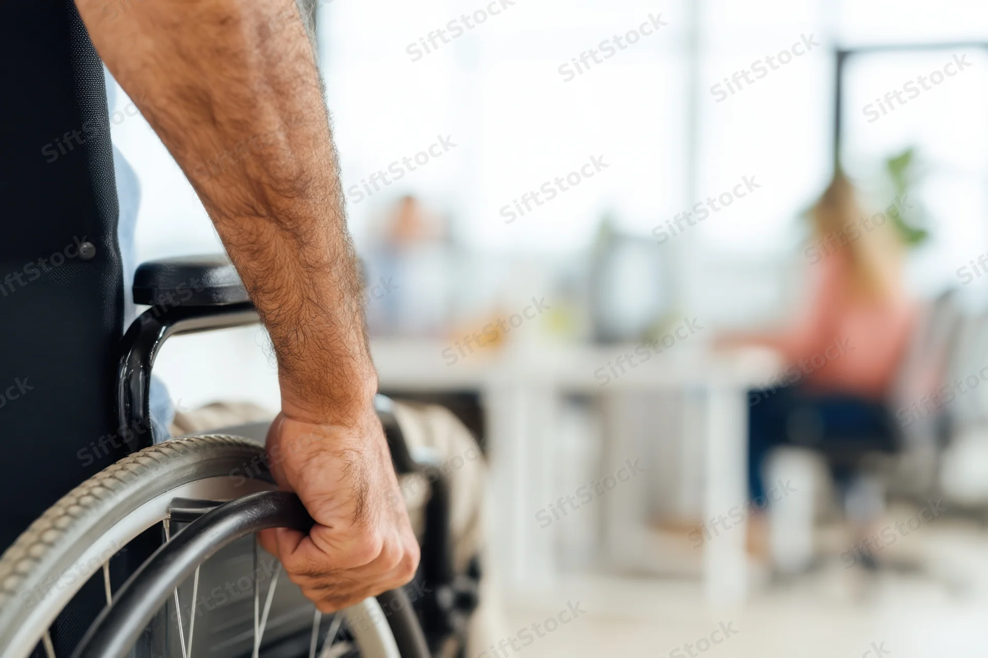 Man’s hand gripping wheelchair wheel in office setting