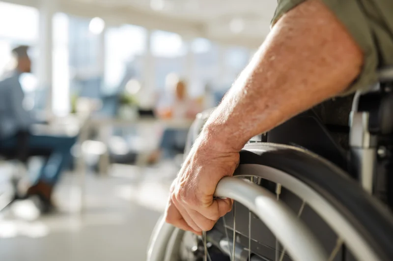 Close-up of a man’s hand gripping a wheelchair wheel in an office setting
