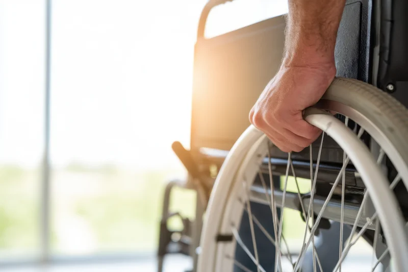 Man’s hand gripping wheelchair wheel indoors near window