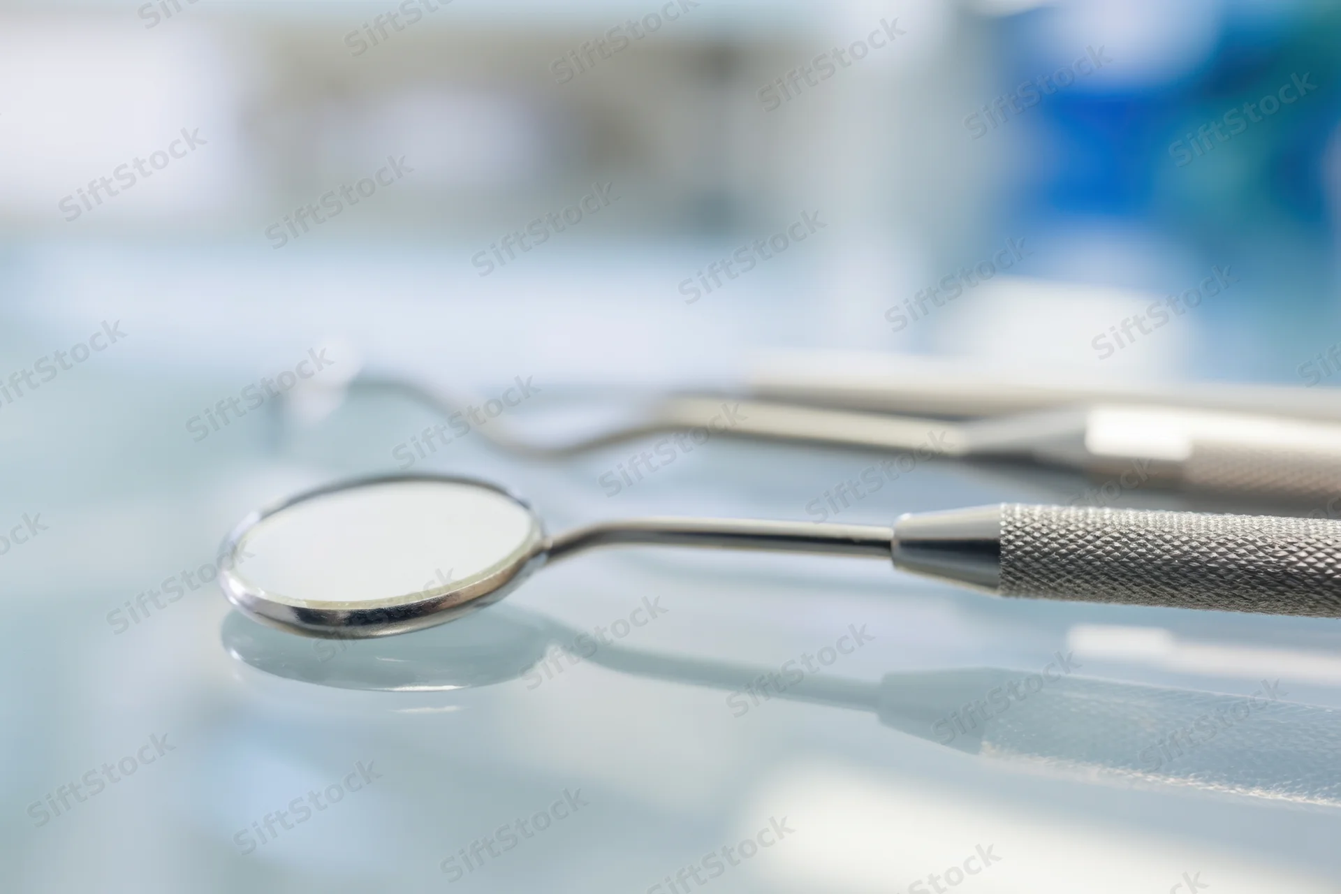 Dental mirror and explorer resting on a reflective surface in a clinic setting