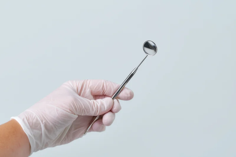 Gloved hand holding a dental mirror against a plain background