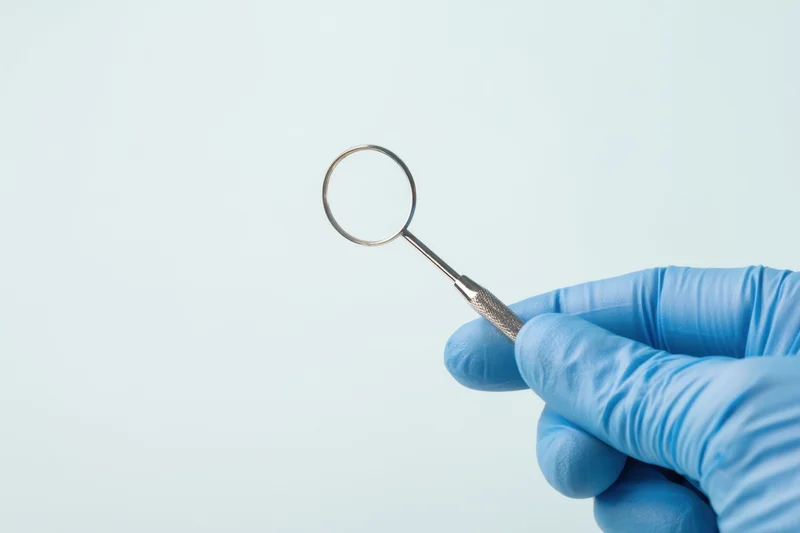 Gloved hand holding dental mirror against light background