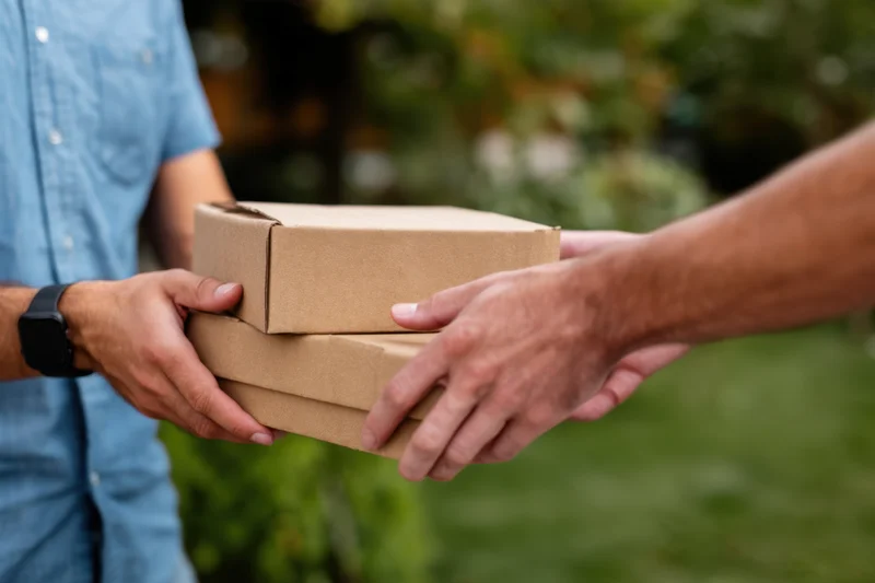 Hands exchanging cardboard boxes outdoors during a delivery
