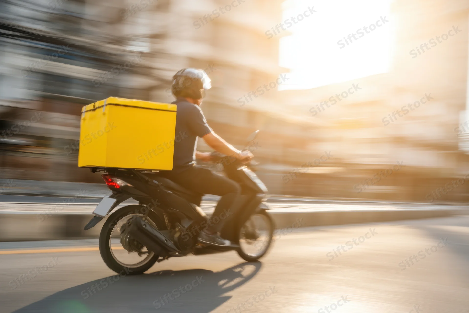 Delivery rider on motorcycle moving through city street at golden hour
