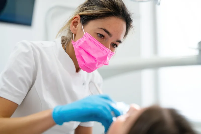 Female dentist wearing a pink mask performing dental work