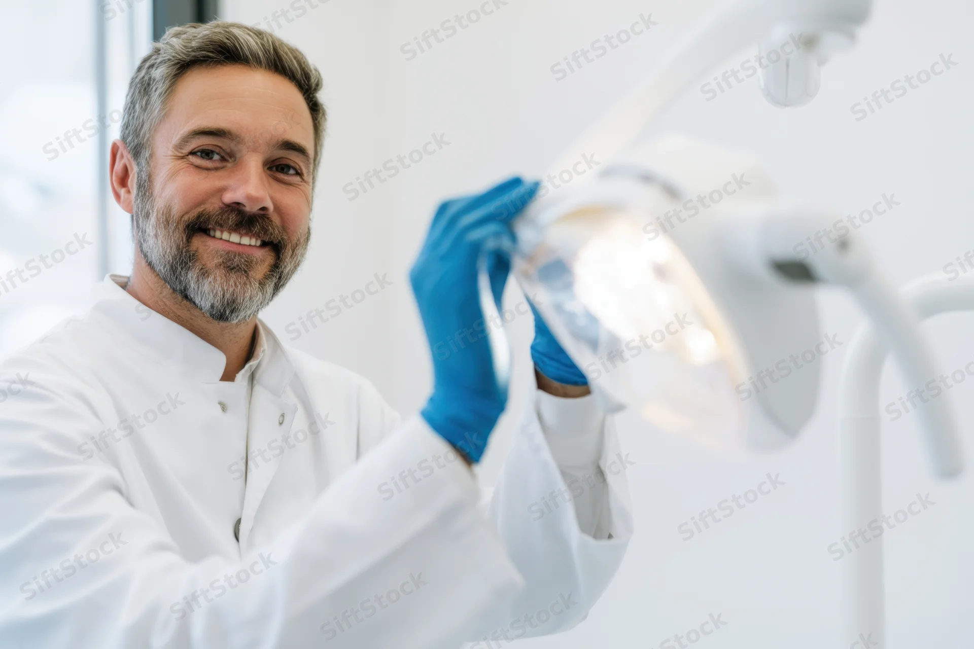 Smiling male dentist adjusting dental lamp in clinic