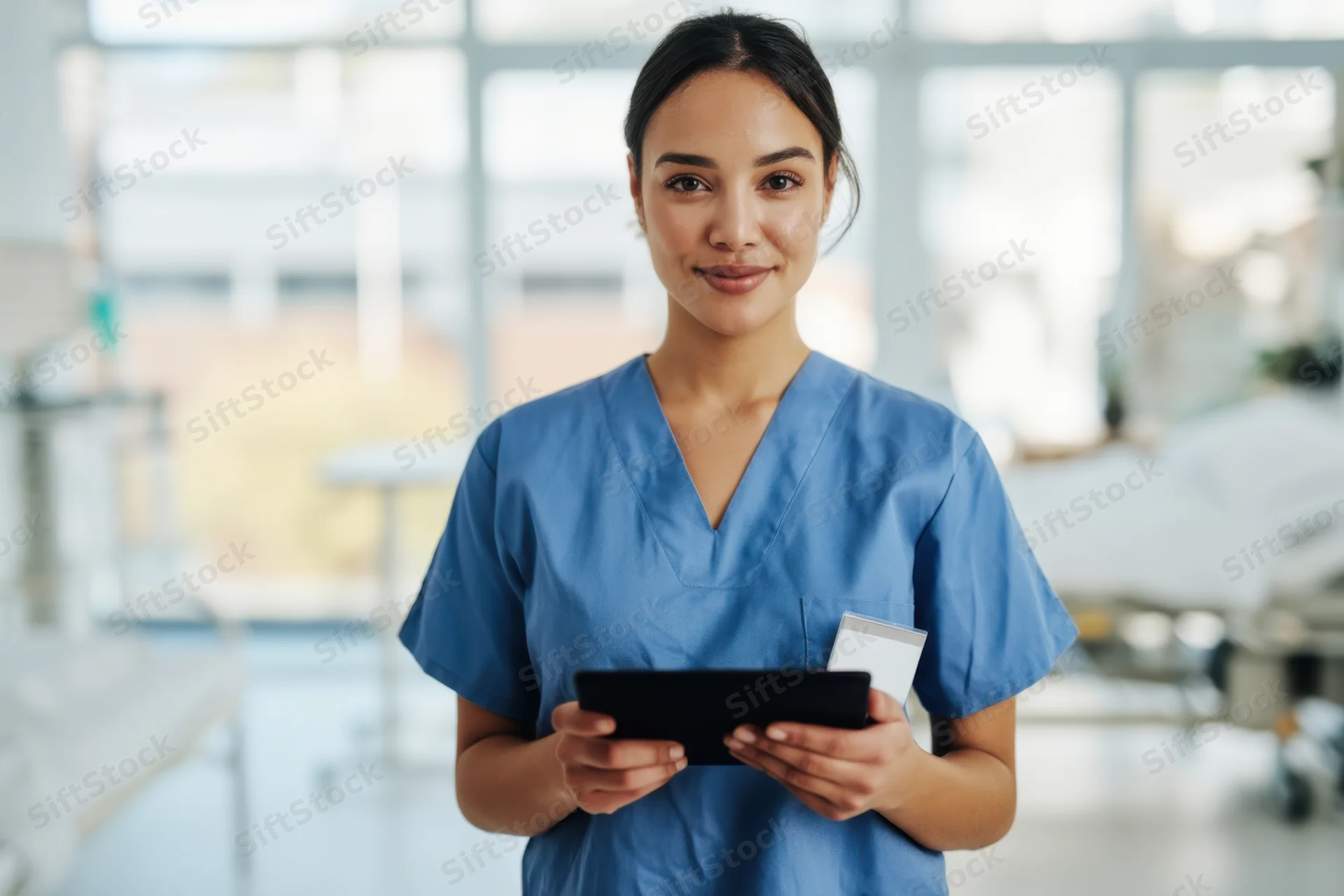 Young asian woman in blue scrubs holding tablet in hospital room