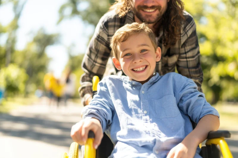 Smiling boy in wheelchair being pushed by father in park
