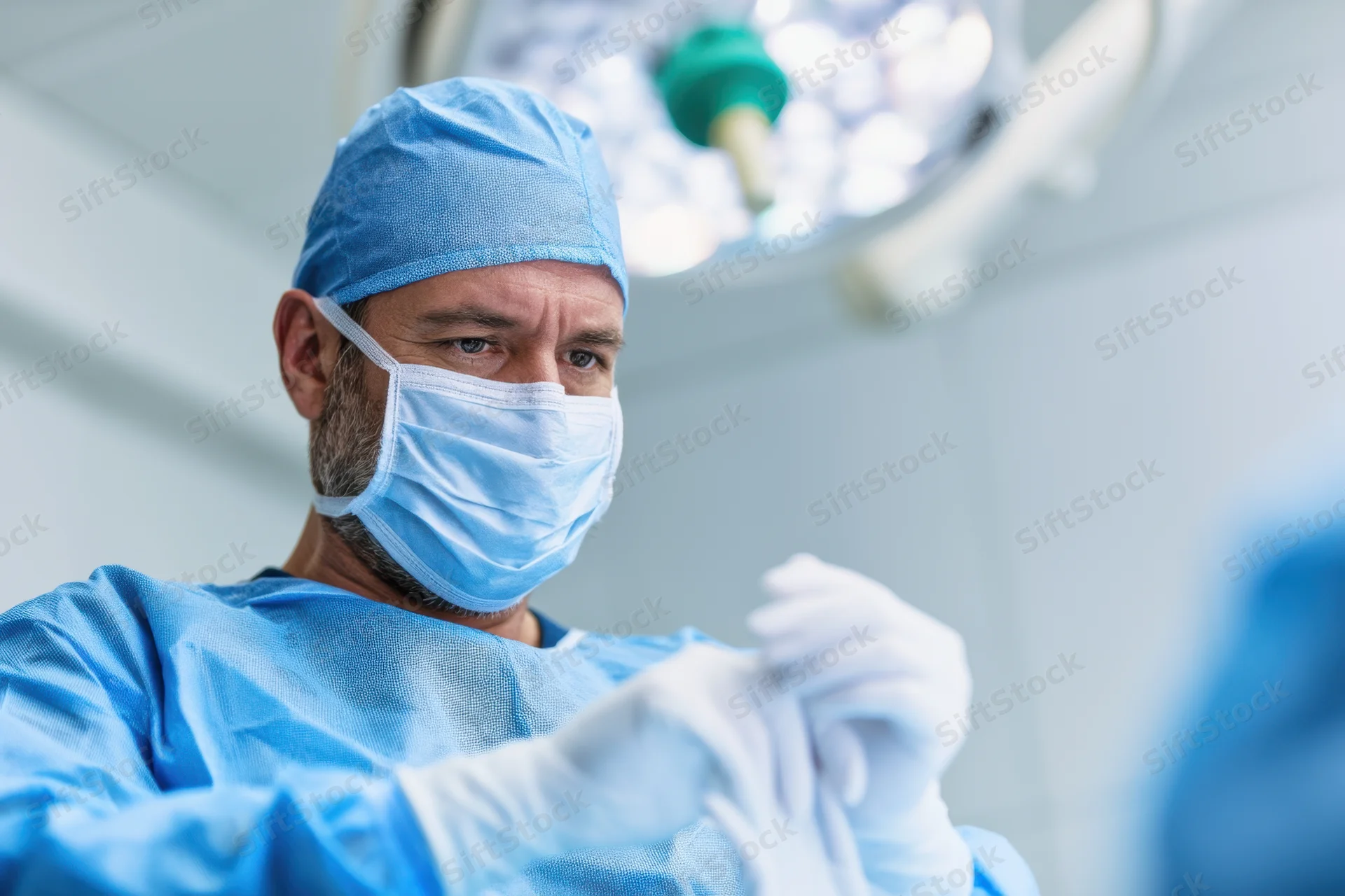 Male surgeon in blue scrubs putting on surgical gloves in operating room