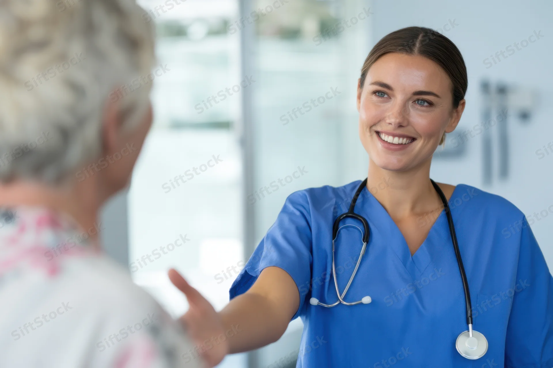Nurse in blue scrubs smiling while interacting with an elderly patient in a clinic