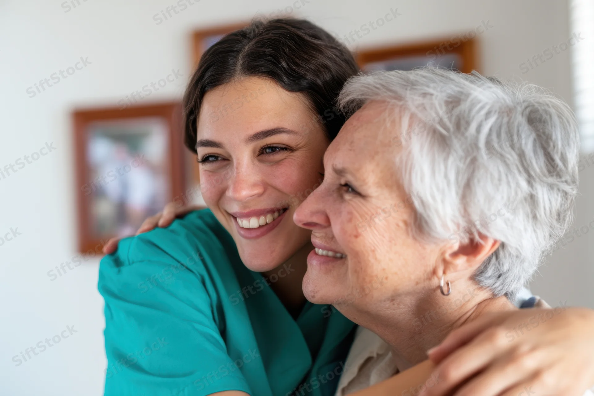 Nurse in teal scrubs hugging senior woman in a home setting