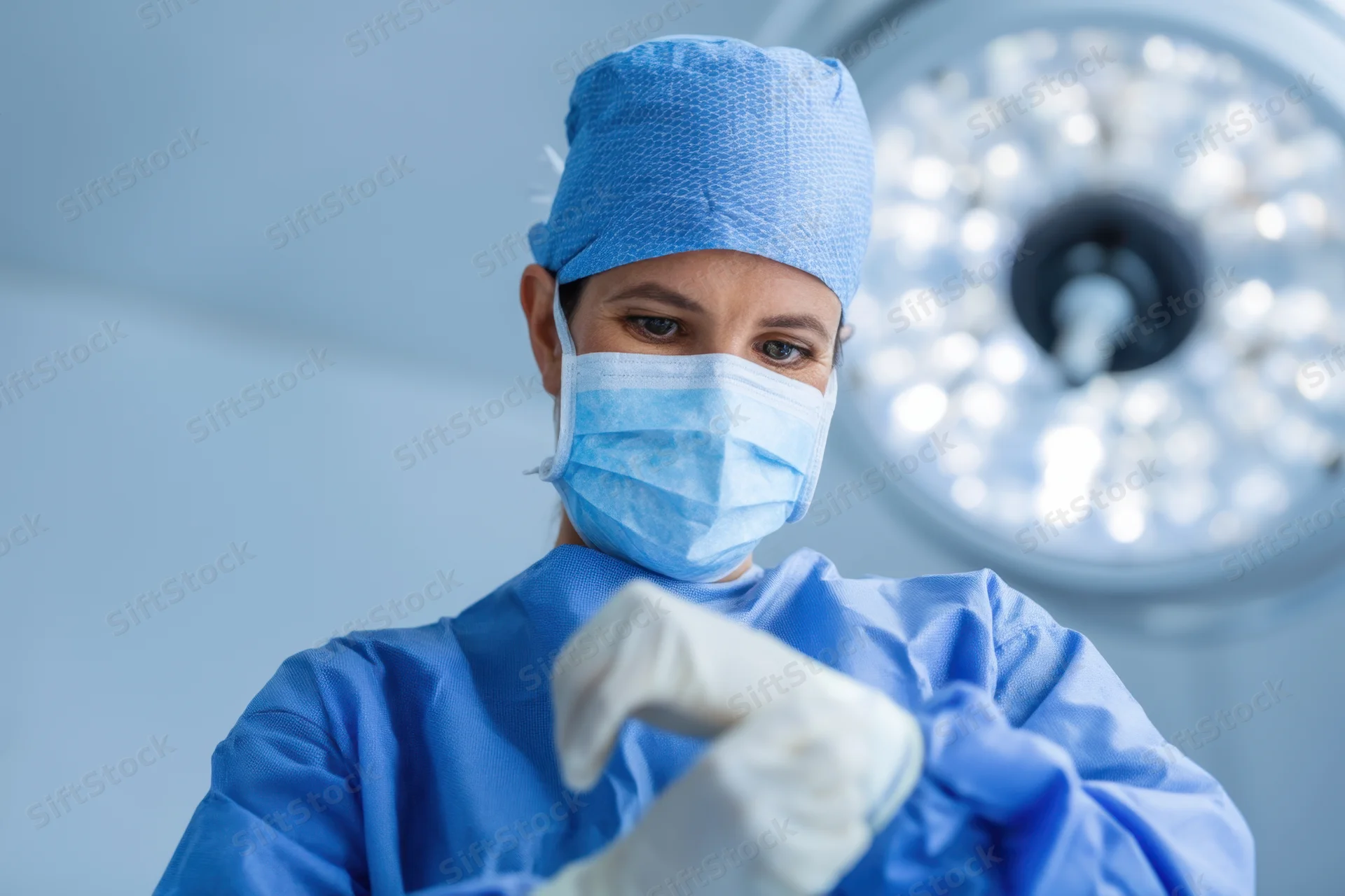 Woman surgeon in blue scrubs putting on gloves in operating room