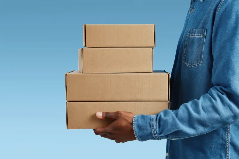 Man holding stack of cardboard boxes against blue background