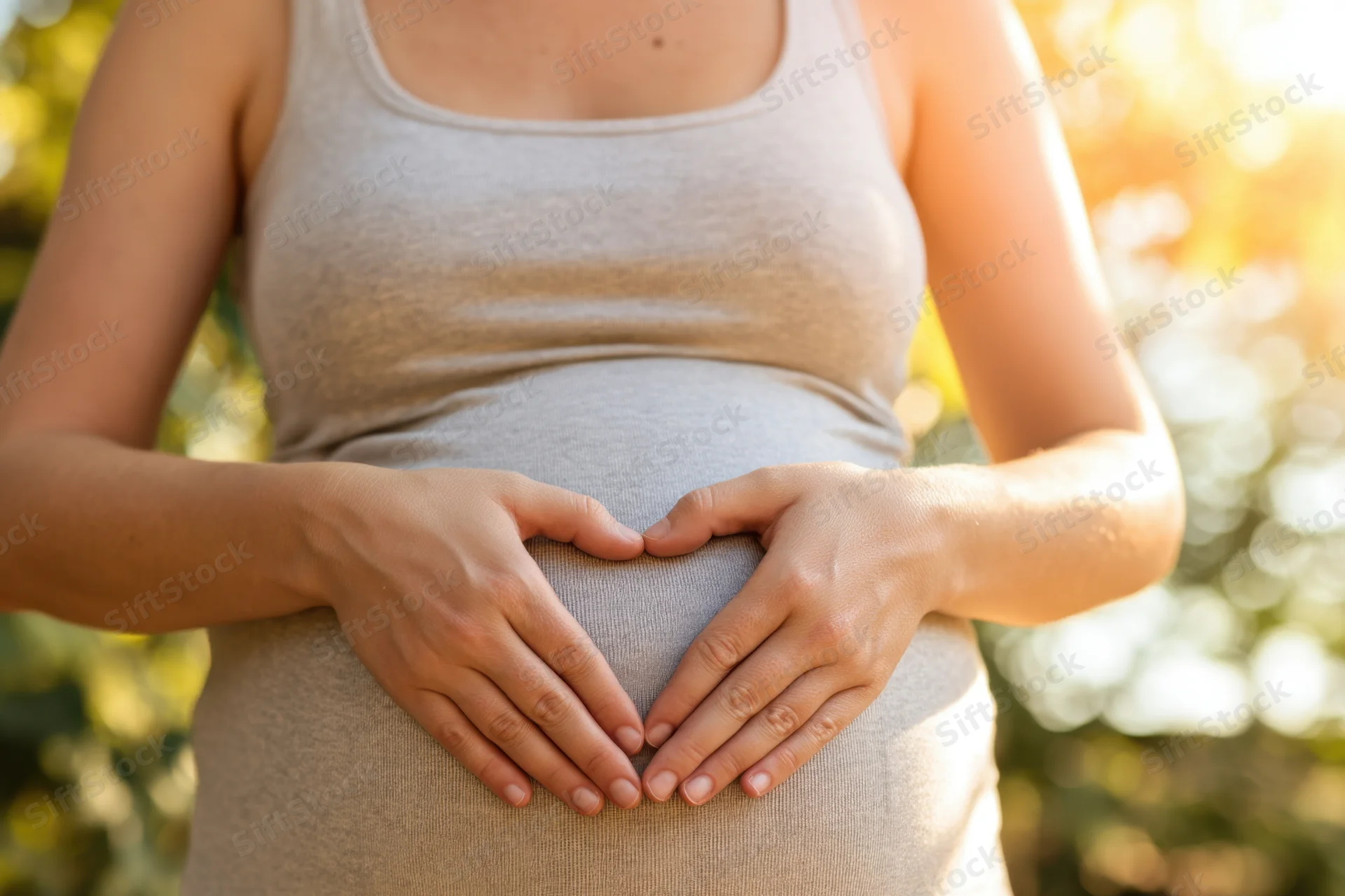 Pregnant woman forming heart shape with hands on her belly outdoors