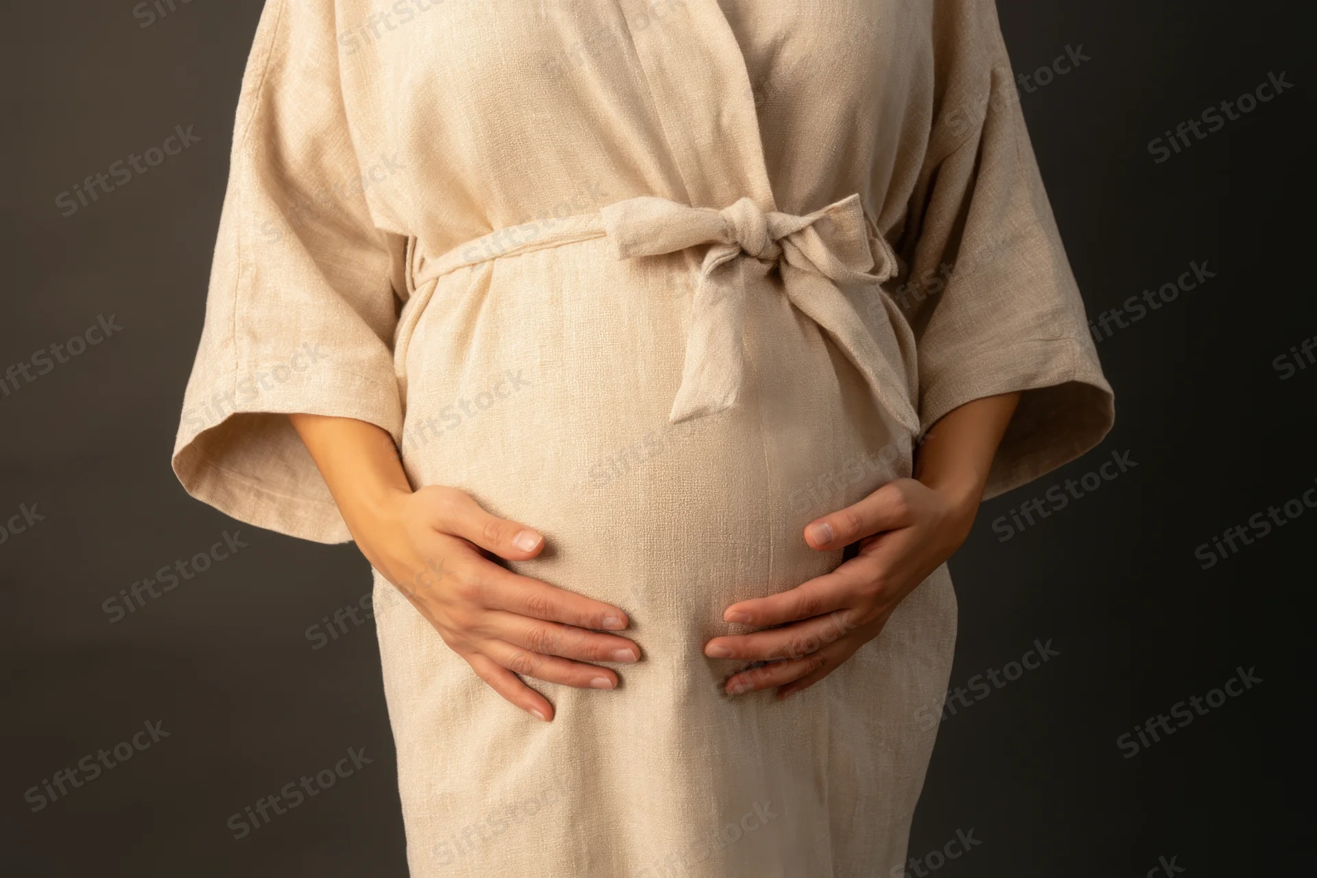 Pregnant woman cradling her belly with hands in a beige linen robe