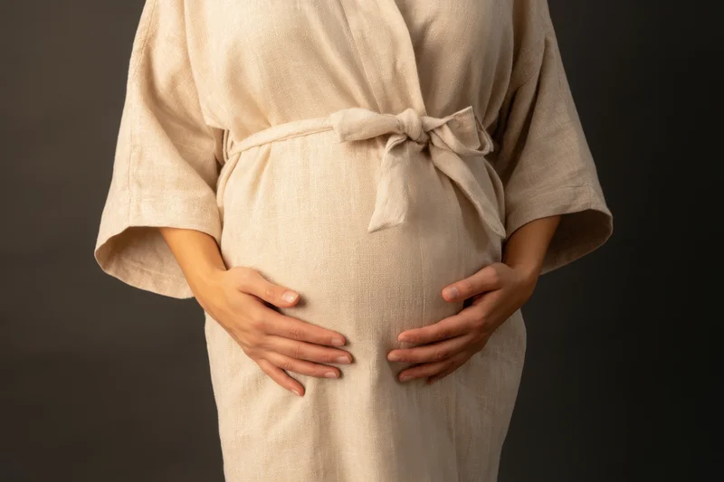 Pregnant woman cradling her belly with hands in a beige linen robe