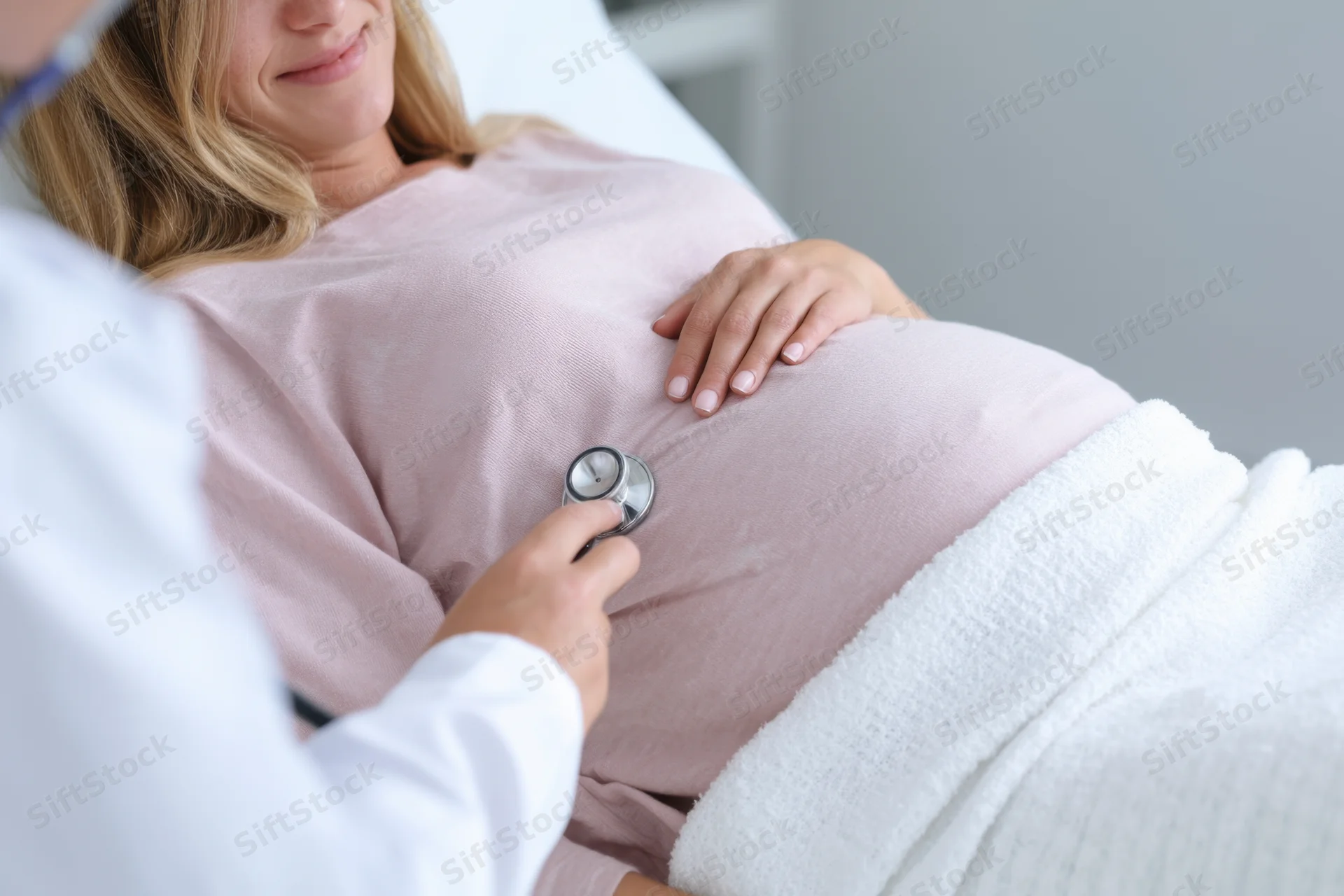 Pregnant woman lying on examination table with doctor using stethoscope on her belly