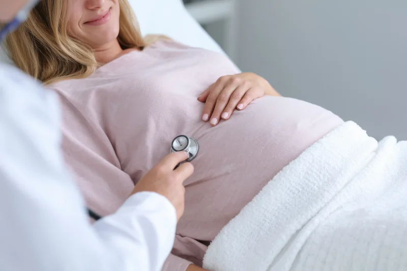 Pregnant woman lying on examination table with doctor using stethoscope on her belly