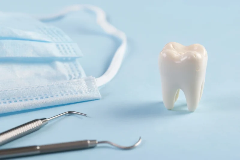 White tooth model with dental tools and mask on blue surface