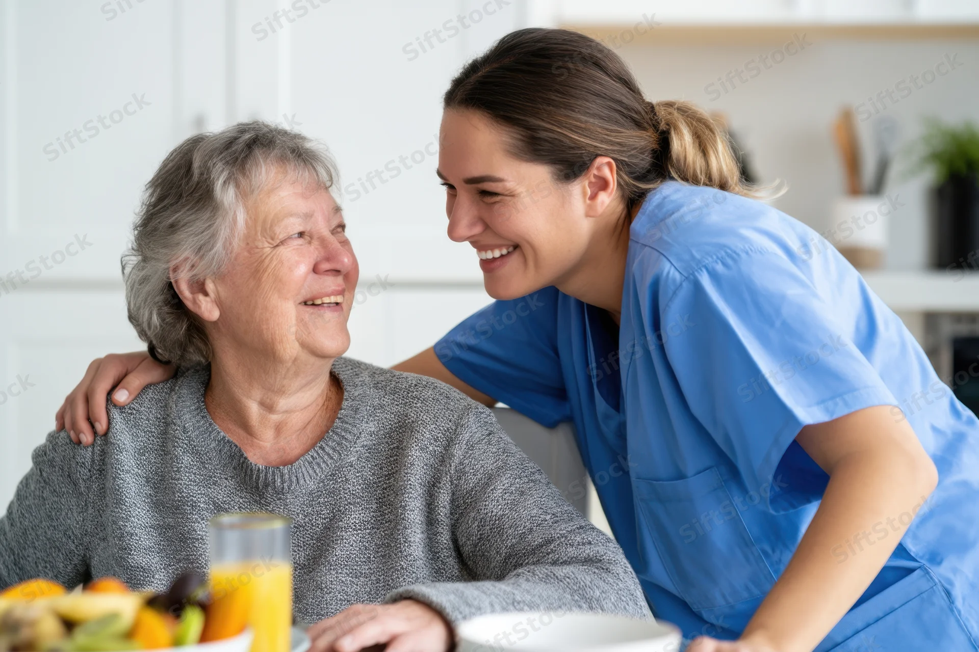 Caregiver smiling with senior woman at kitchen table during breakfast
