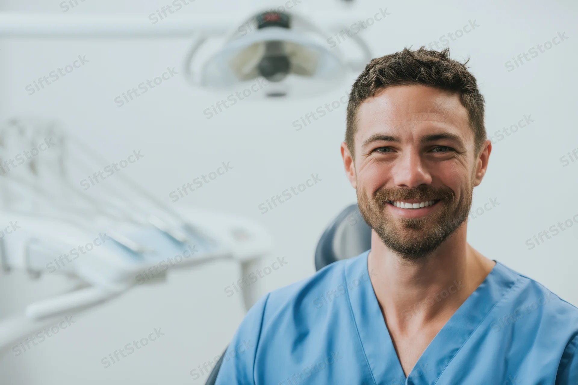 Smiling male dentist in blue scrubs in a dental clinic office