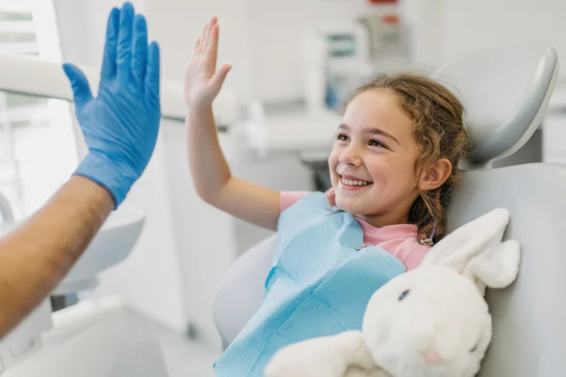 Young girl smiling and high-fiving dentist in dental chair with stuffed rabbit