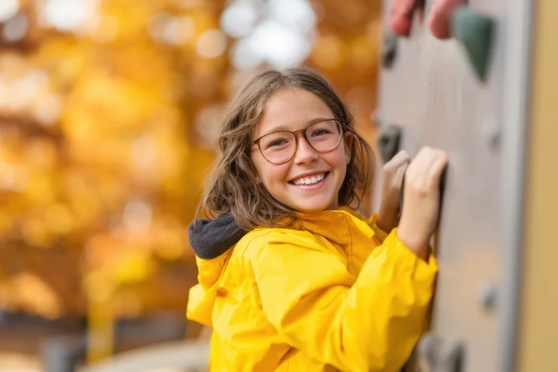 Smiling girl in yellow jacket climbing playground wall outdoors in autumn