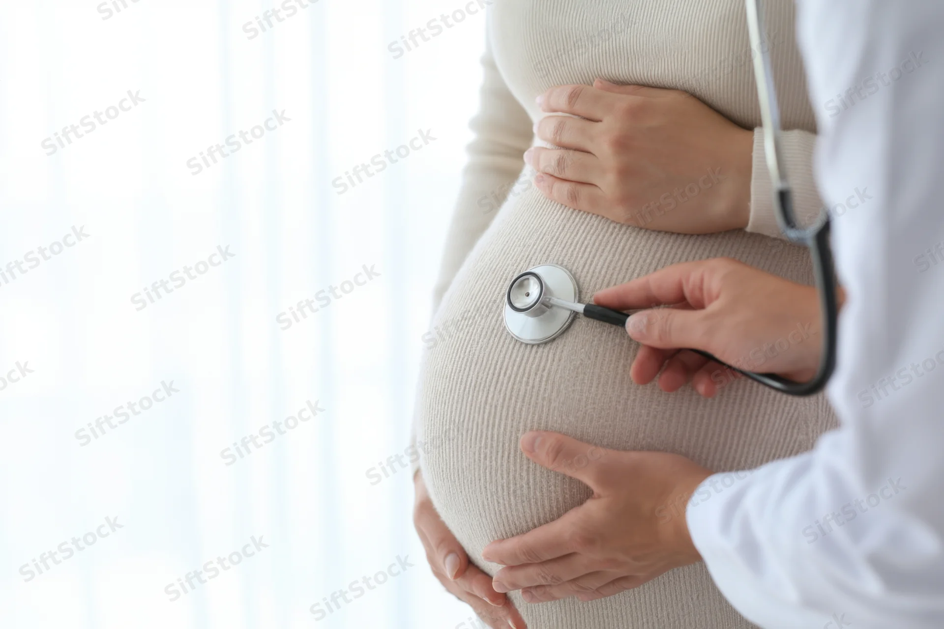 Doctor examining pregnant woman's abdomen with stethoscope in clinic