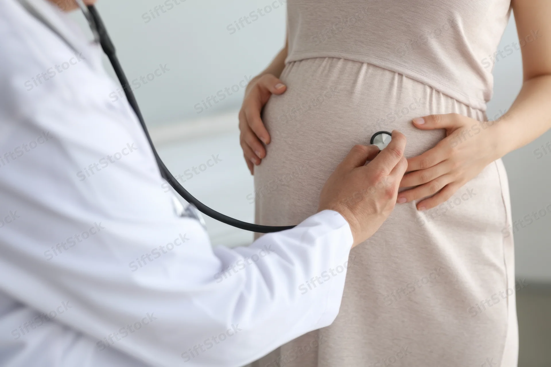 Doctor examining pregnant woman's belly with stethoscope in clinic