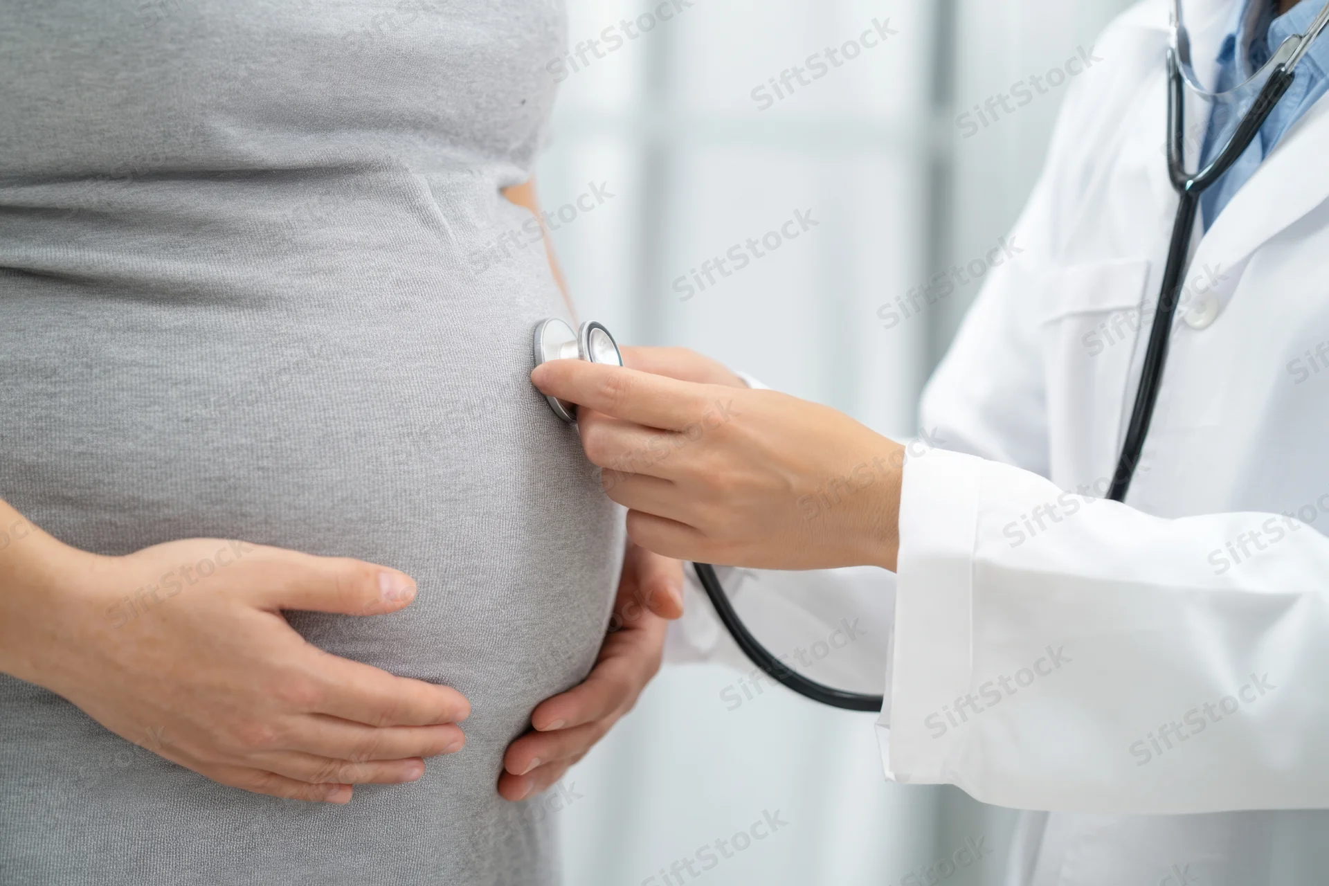 Doctor using stethoscope on pregnant woman's belly in clinic