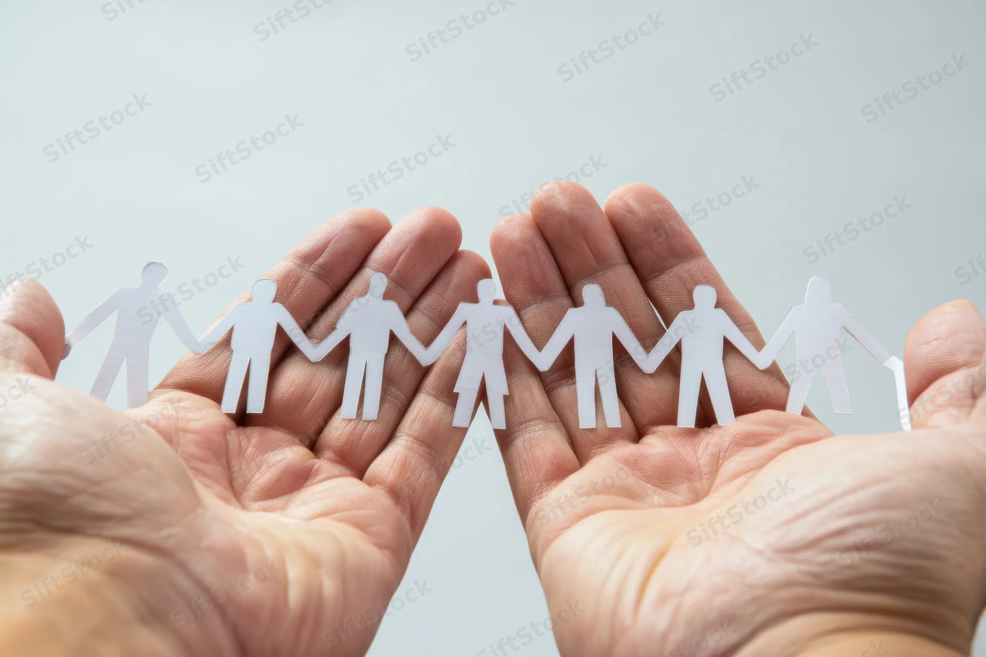 Open hands holding a chain of white paper cutout figures symbolizing human connection and teamwork