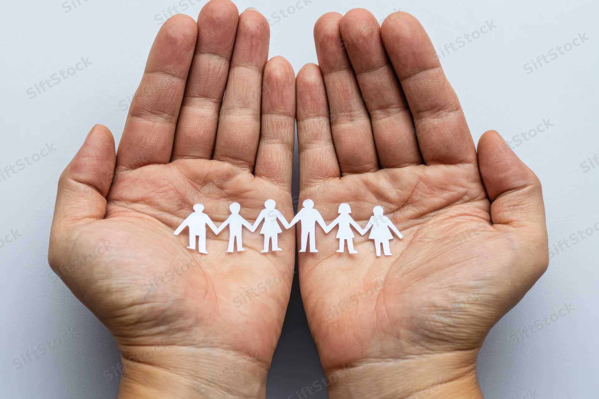 Open hands holding a paper cutout family of six figures in a line