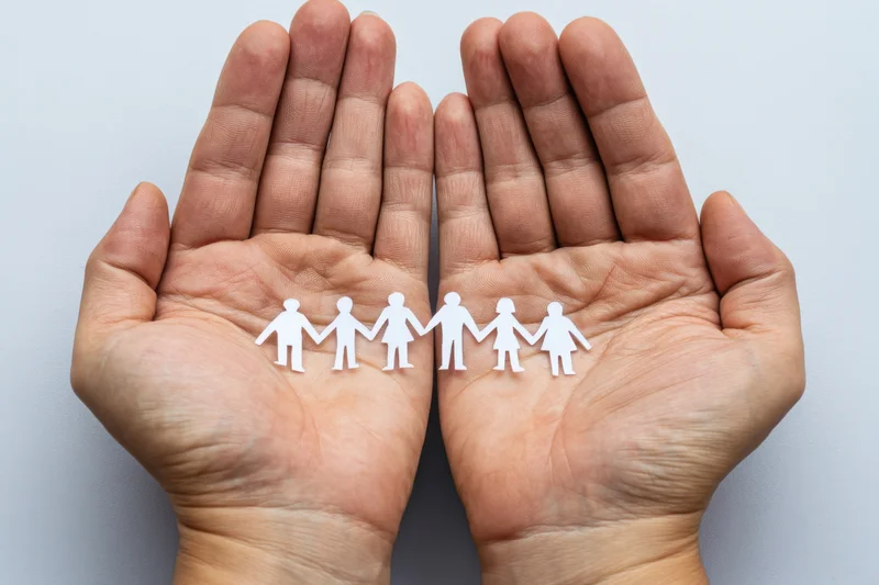 Open hands holding a paper cutout family of six figures in a line