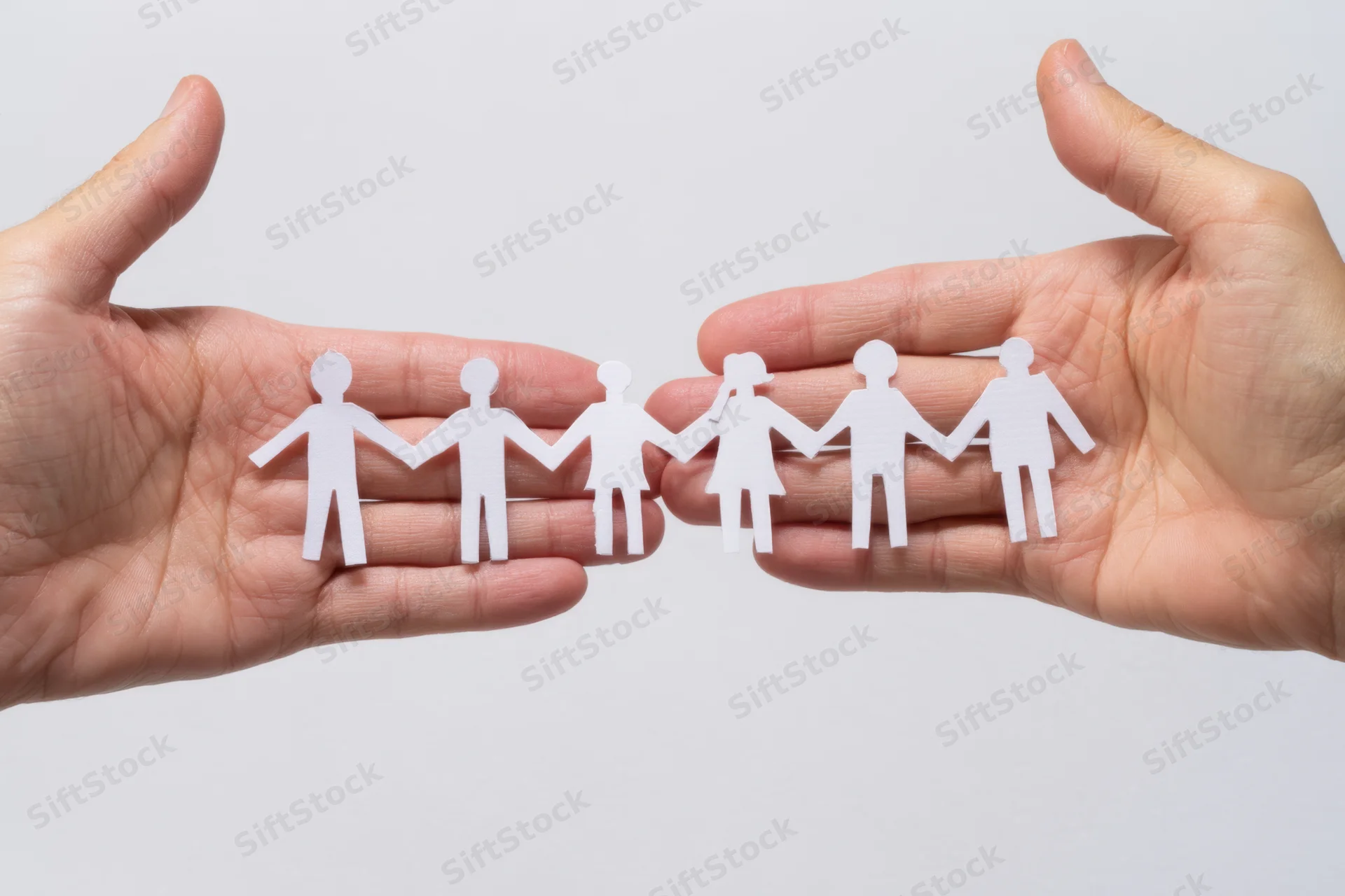 Open hands holding a chain of white paper cutout figures in a line