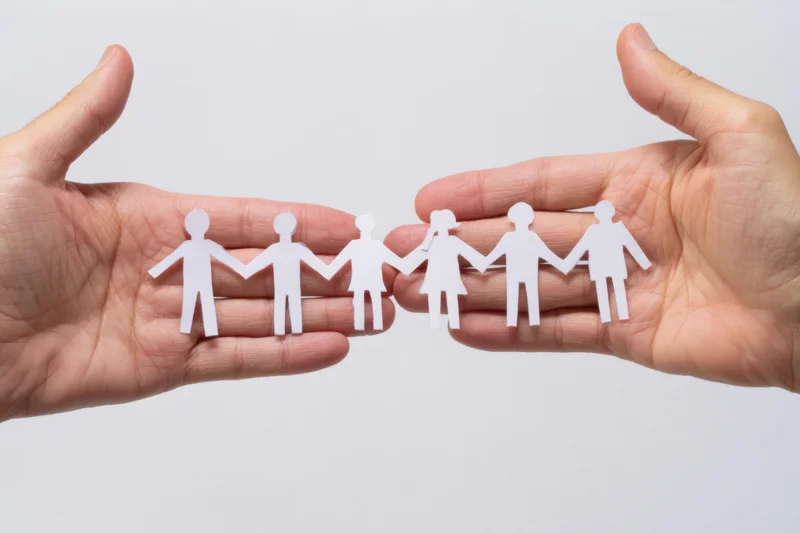 Open hands holding a chain of white paper cutout figures in a line