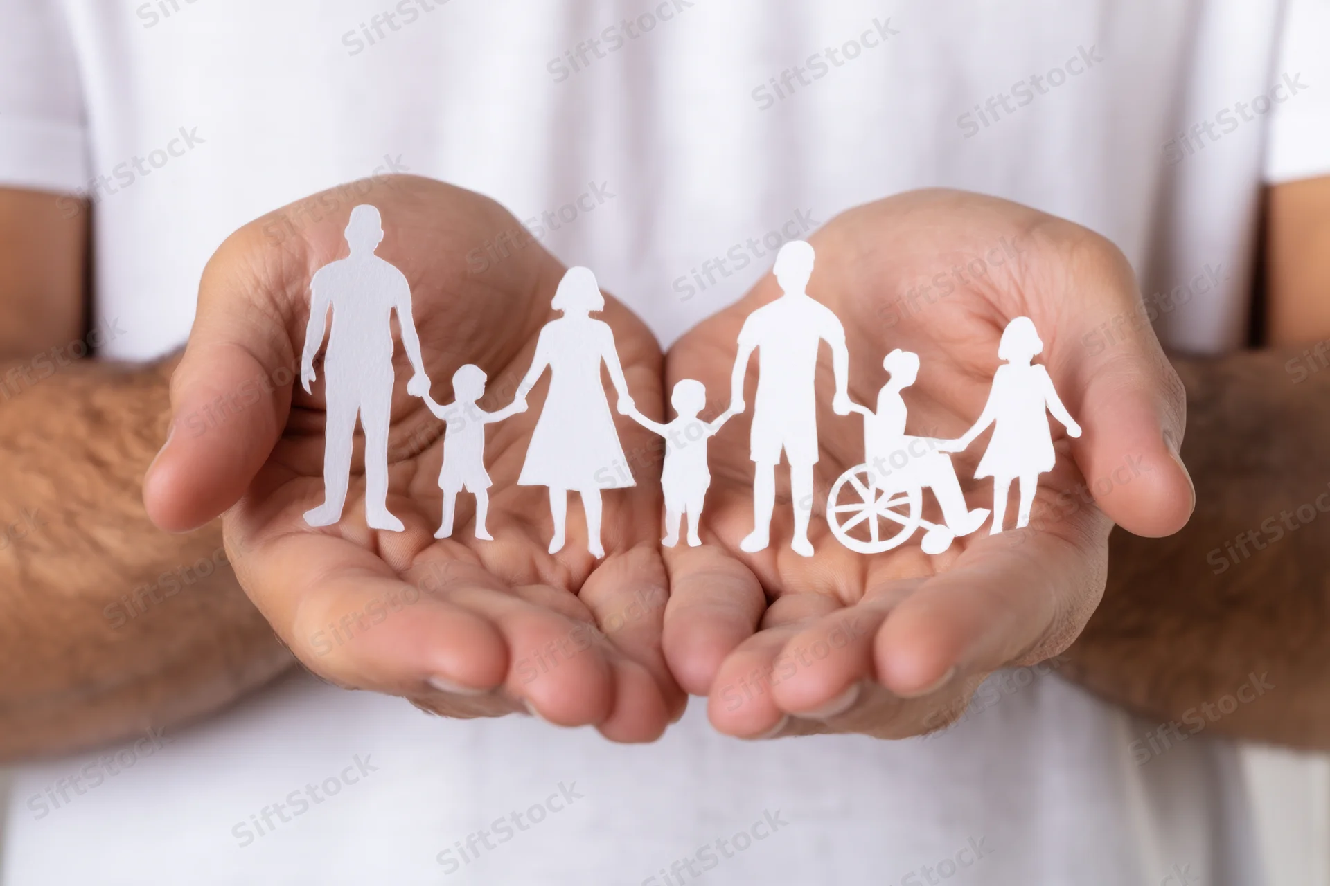 Hands cradling white paper cutouts of diverse family figures including a person in a wheelchair