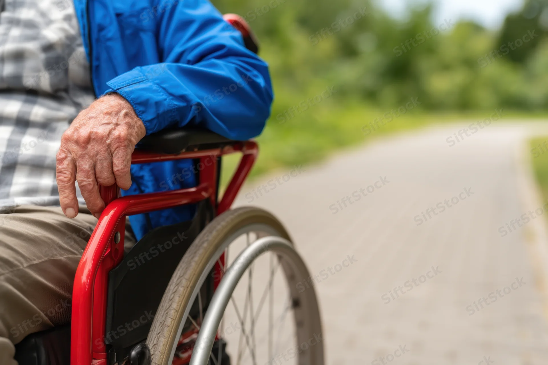 Senior man in red wheelchair gripping handle on paved outdoor path