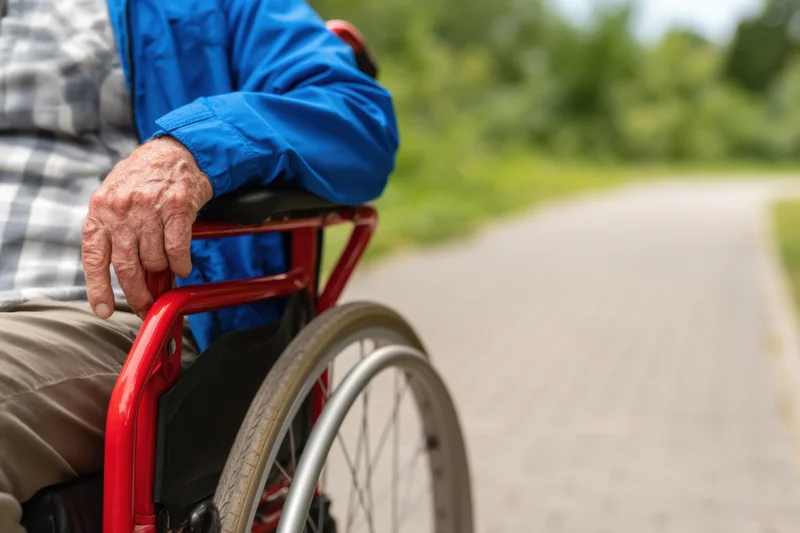 Senior man in red wheelchair gripping handle on paved outdoor path
