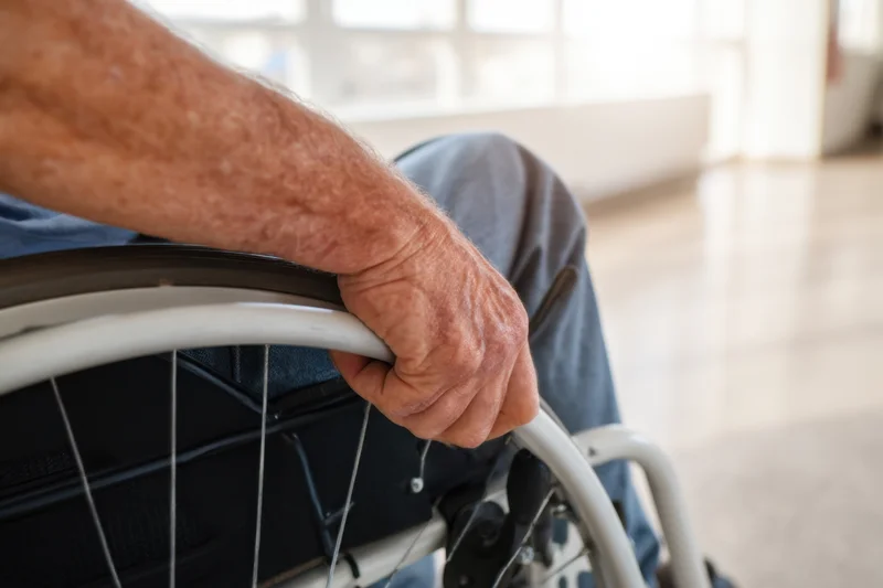 Close-up of a senior man's hand gripping the wheel of a wheelchair indoors