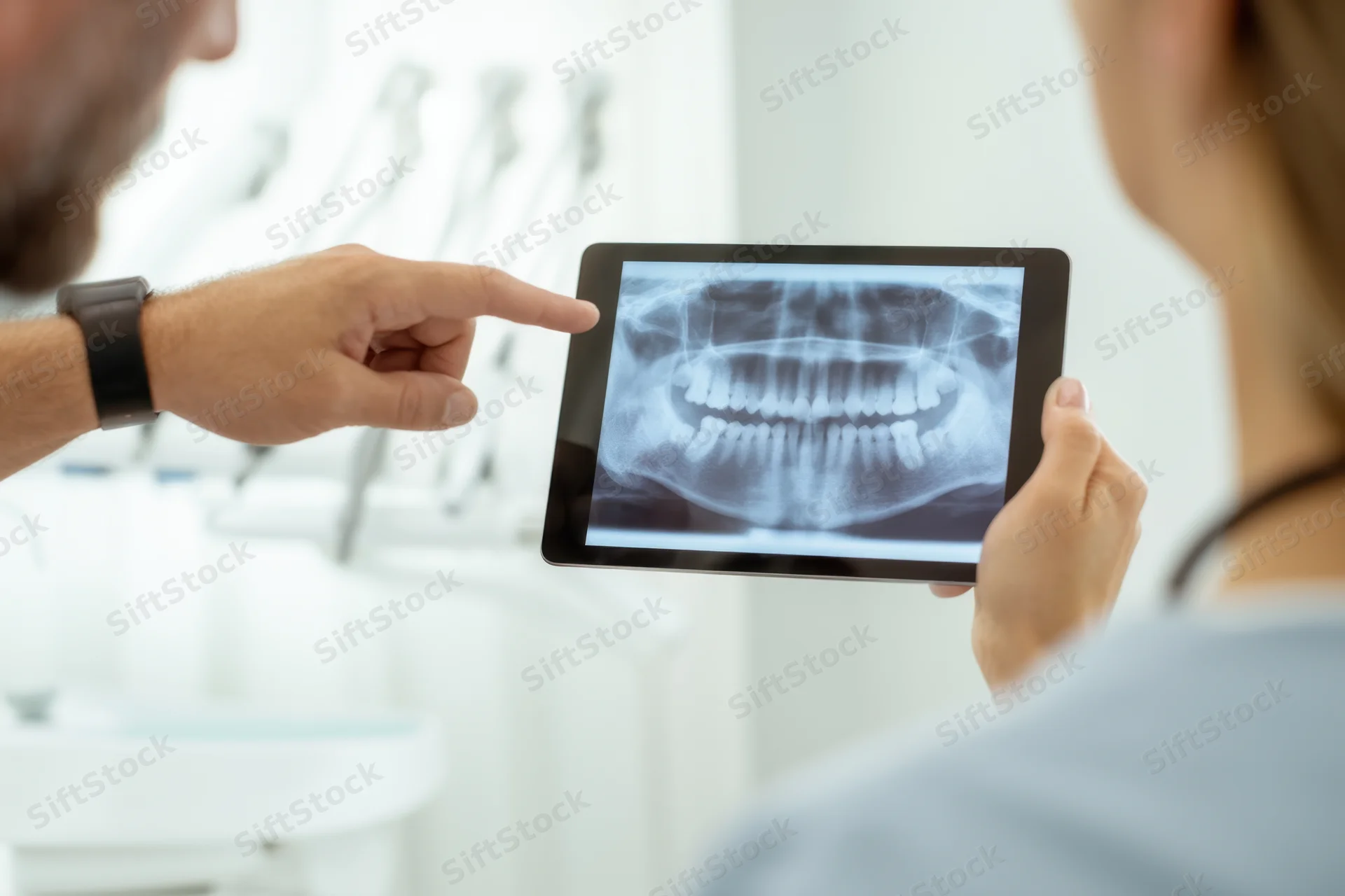 Dentist pointing at dental xray on tablet during patient consultation in clinic