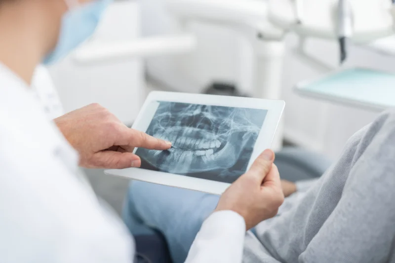 Dentist pointing at dental xray on tablet during patient consultation in clinic